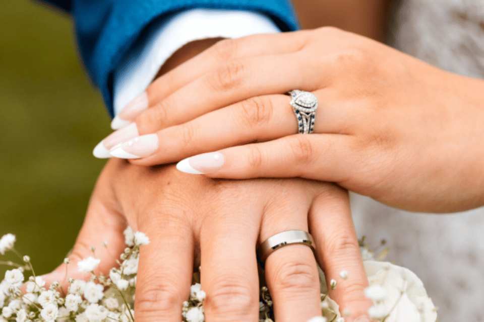 Diamond and engagement rings Columbus, OH - a bride's hand with a diamond engagement ring and wedding band on top of a groom's hand