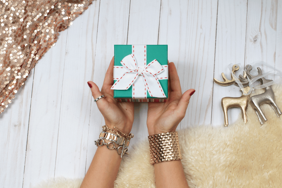 Gift Guide for Her - Elizabeth Diamond Company - woman holding a gift box wearing  a ring and bracelets